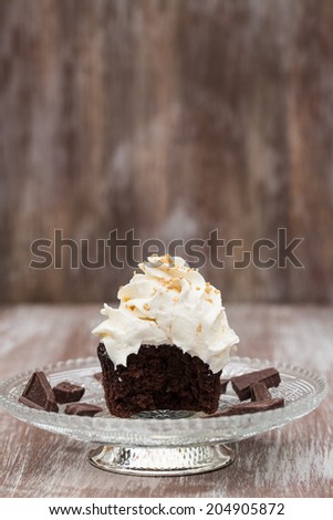 Chocolate cupcake with vanilla frosting missing a bite on antique glass plate with chocolate pieces