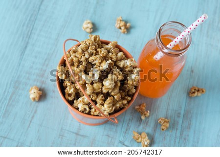 Caramel popcorn in orange tin bucket with orange soda pop with straw from above
