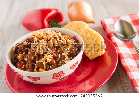 Bowl of warm chili winter comfort food dinner with corn bread muffin and red pepper and onion