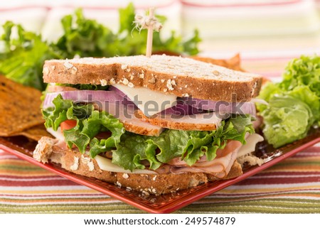 Lunch sandwich of ham turkey cheese lettuce tomato with chips on plate