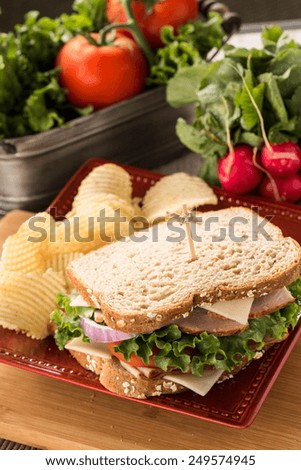Sandwich with ham and turkey for lunch with potato chips and vegetables