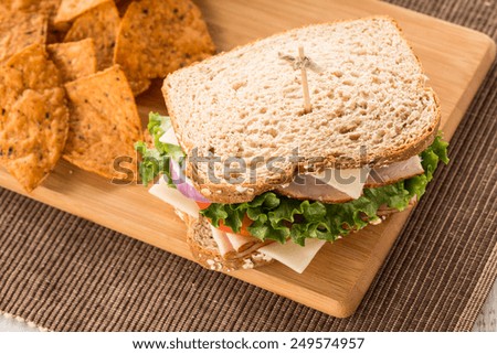 Ham turkey and swiss cheese and onion sandwich with tomato and lettuce and chips on wood board