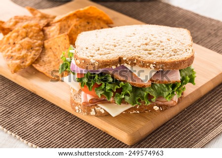 Healthy lunch sandwich with ham turkey lettuce tomato onion and swiss cheese on a cutting board with chips