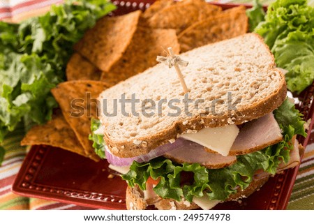 Lunch sandwich with turkey ham and lettuce and chips on a red plate