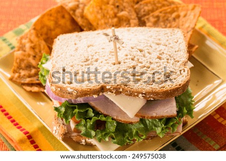 Turkey and ham sandwich on wheat bread with chips close up