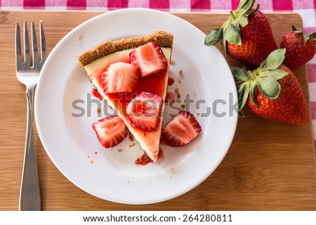 Photograph of a slice of fresh cheesecake with fresh cut strawberries on a white plate from above