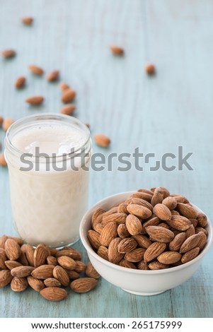 Almonds in white bowl on blue wood background with glass of almond milk vertical