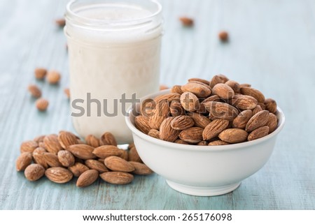 Almonds in white bowl on blue wood background with glass of almond milk