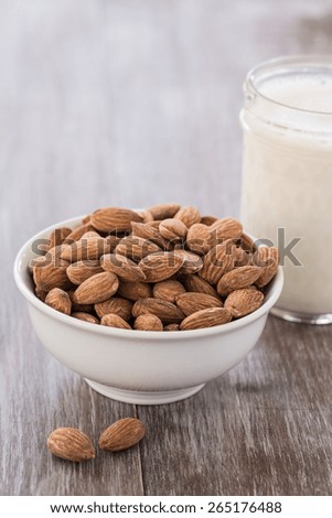 A white bowl of almonds and a glass of almond milk on wood background