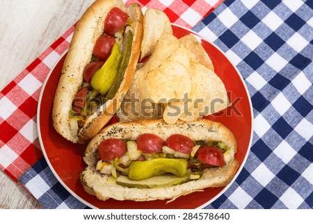 Two Chicago style hot dogs on a red plate with potato chips