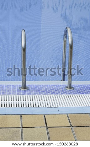 Turquoise blue water in pool with tiles and metal ladders, fun