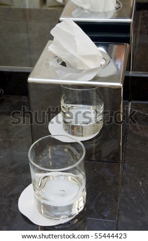Multiple reflections of glass and disposable paper napkin holder in mirror