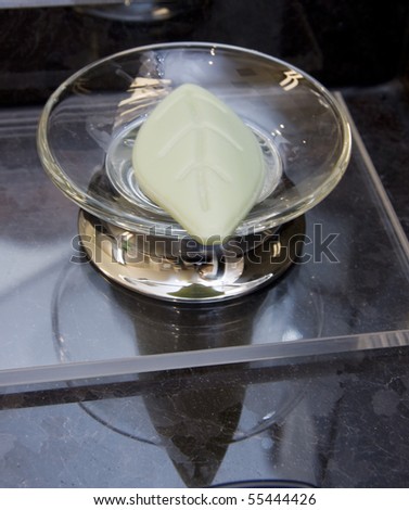 Bar of soap in leaf form in glass soap-dish on black marble background