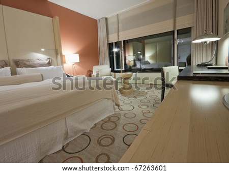 Room with king-size bed bedside table chair  lamps desktop and reflection in large window
