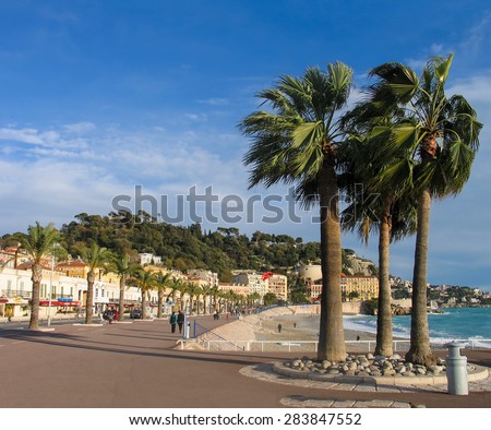NICE, FRANCE - DECEMBER 05, 2005: People take a walk on winter day at pedestrians on Promenade des Anglais with palm trees in Nice, France on December 05, 2005.