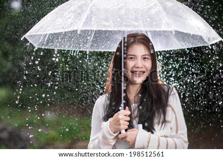 Happy Asian girl with transparent umbrella among the rain
