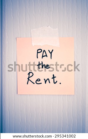 sticky note write a message pay the rent on wood door background vintage style