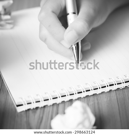 woman hand writing with pen on notebook.there are crumpled paper and coffee cup on wood table background black and white color tone style