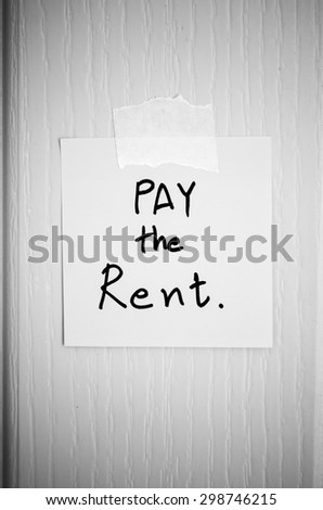 sticky note write a message pay the rent on wood door background black and white color tone style