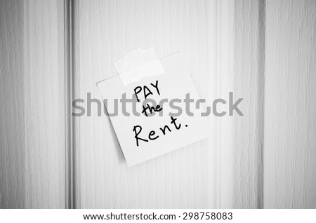 sticky note write a message pay the rent on wood door background black and white color tone style