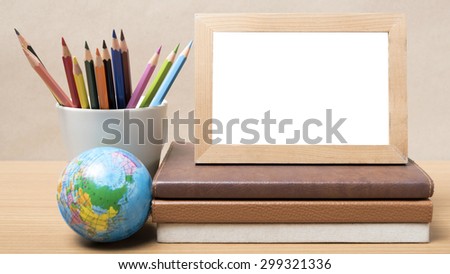 stack of book photo frame with color pencil and earth ball on wood background