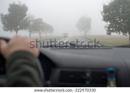 Car driving in thick fog, seen through windscreen of other vehicle