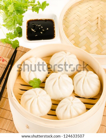 Chinese steamed buns in bamboo steamer basket with cilantro, soy sauce over the bamboo mat