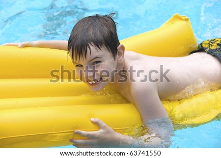 Happy young boy relaxing at the swimming pool on a yellow lilo