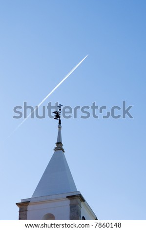 Belfry tower with an angel weather vane pointing to the sky cruise by a jet plane