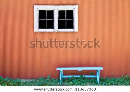 Empty blue bench on orange wall with window