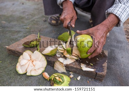 Man peeling coconut fruit with knife