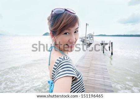 A happy Asian girl on a wooden bridge in a sea