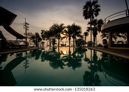 dawn at early morning over peaceful still swimming pool with palm silhouettes in summer resort in thailand