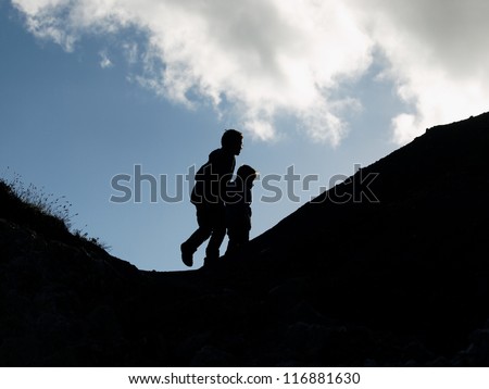 Two boys playing outside, climbing up a hill, silhouette