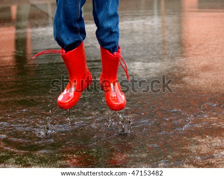 child with rain boots jumps into a puddle