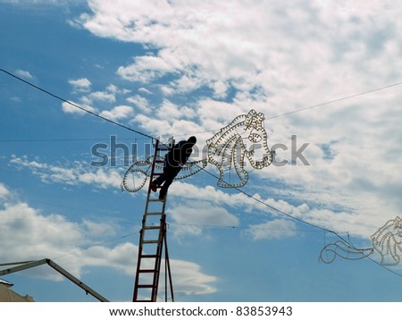 electrician on a high ladder connecting fair illuminations , doing a dangerous job at high altitude
