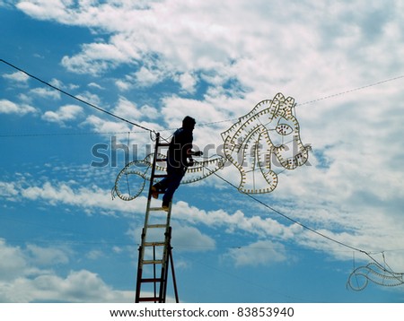 electrician on a high ladder connecting fair illuminations , doing a dangerous job at high altitude