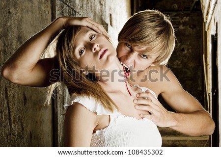 Male vampire bites blonde woman, her neck is bleeding from a bite wound