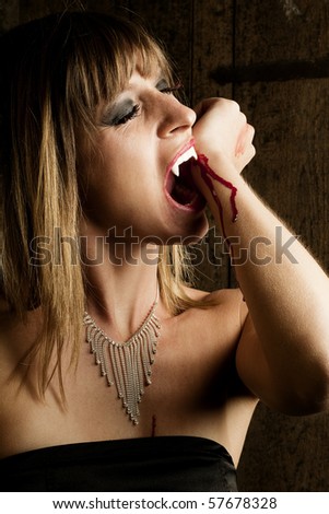 Female, blonde Vampire is biting her wrist to feed a human to be transformed into a Vampire. Taken in an old Viennese cellar.