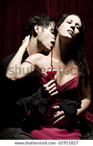 A male Vampire is sucking the blood of his female prey and holding a glass below, where the spilled blood is flowing down.