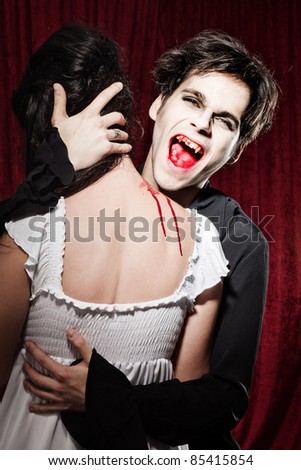 Male vampire has bitten a young woman\'s neck and got caught. He is showing his bloody teeth.