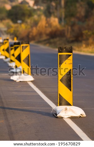 Caution road signs held up by sand bags on a tarred road