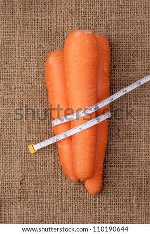 A tape measure wrapped with a carrot that is placed on a cloth sack.