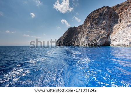 View behind the stern of a boat of the wake rippling over a calm sea when cruising off a tropical island with steep rocky cliffs towering out of the sea