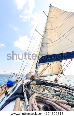 Aboard a yacht on a calm blue ocean with a view of the ropes on the deck, mast, sails and rigging under a clear blue sky on a sunny summer day in the tropics