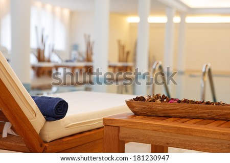 Comfortable adjustable wooden recliner seat with a foam cushion and attached side table standing poolside at an indoor swimming pool at a resort or spa
