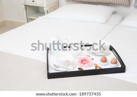 Breakfast in bed for two with a neatly laid tray on the end of a white bed laid with two boiled eggs and coffee with a single romantic pink rose