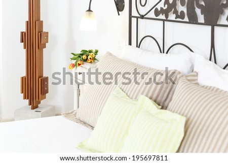 Stylish wrought iron double bed with striped pillows and bedroom decor with a modern wooden sculpture on the wall, close up detail