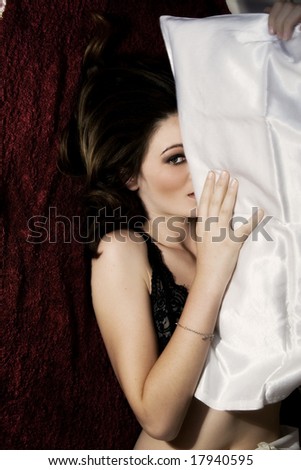 Beautiful woman hiding under a satin pillow
