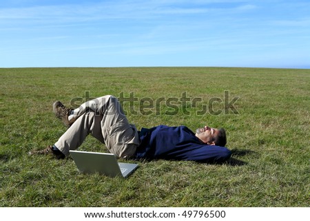 Mature man relaxing in field next to laptop - stock photo